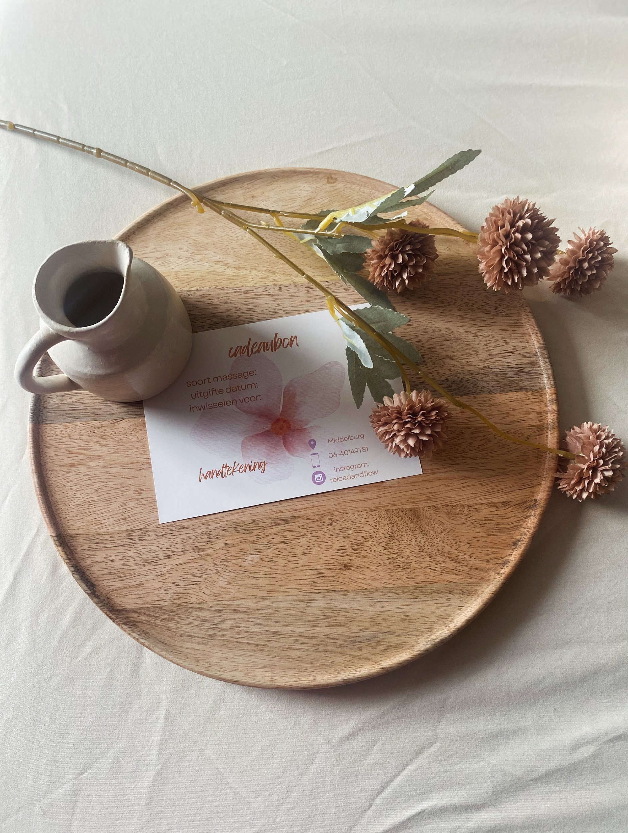 Een cadeaubon van Reload and Flow op een houten dienblad met een kannetje en gedroogde bloemen